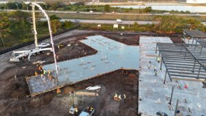 Concrete pump truck placing a commercial building slab beside the steel structure