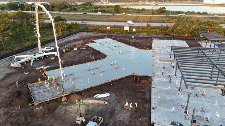 Concrete pump truck placing a commercial building slab beside the steel structure